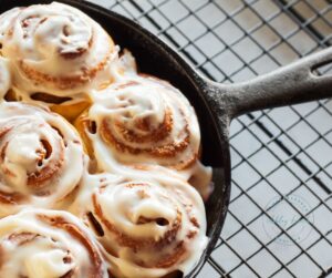 Yeast cinnamon roll recipe served in a cast iron skillet with melted cream cheese icing – cozy farmhouse breakfast fresh from the oven.