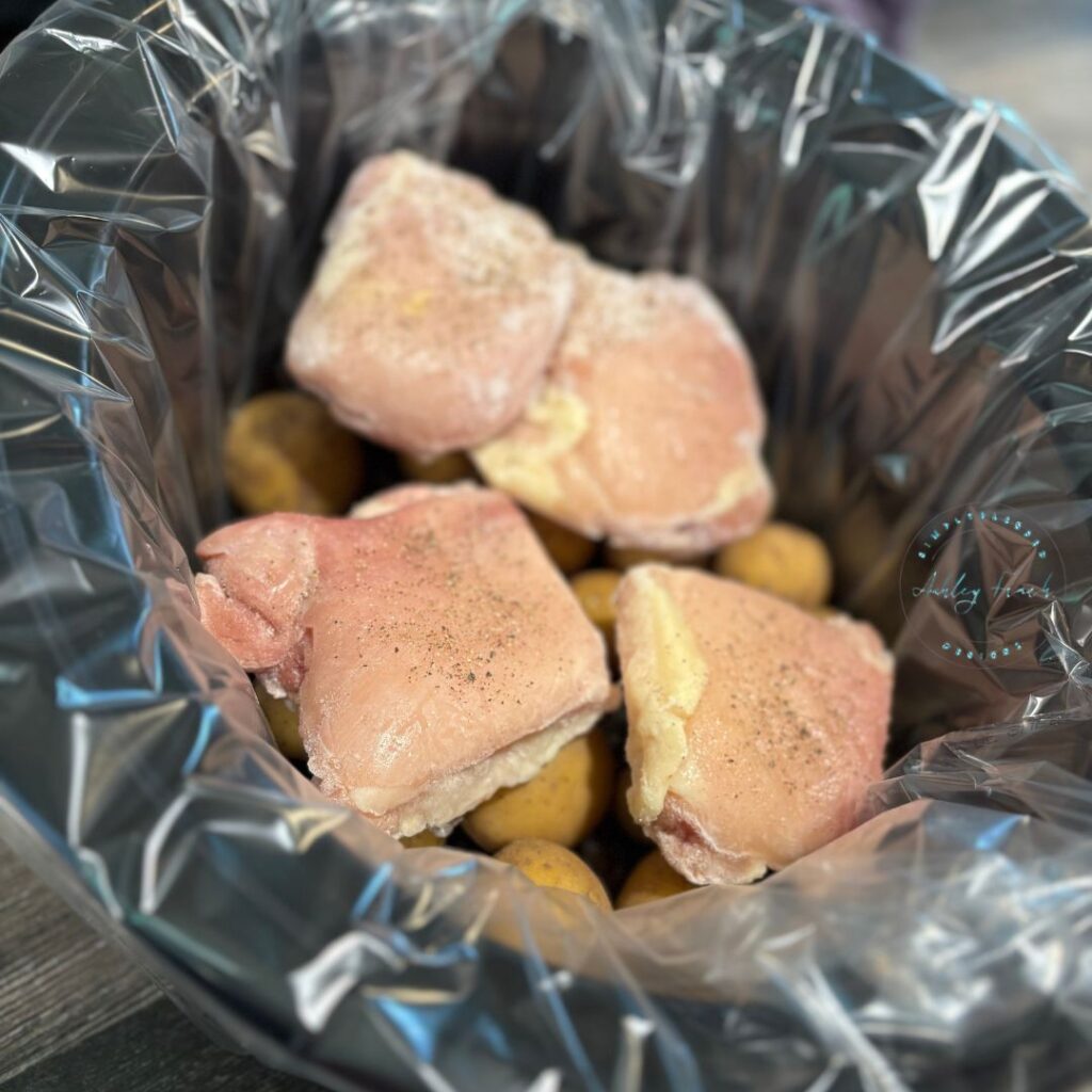 Baby potatoes and frozen chicken thighs layered in a lined crockpot before cooking — easy prep for creamy garlic herb chicken dinner.