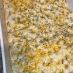Golden sourdough focaccia fresh from the oven, topped with rosemary, cheese and herb salt