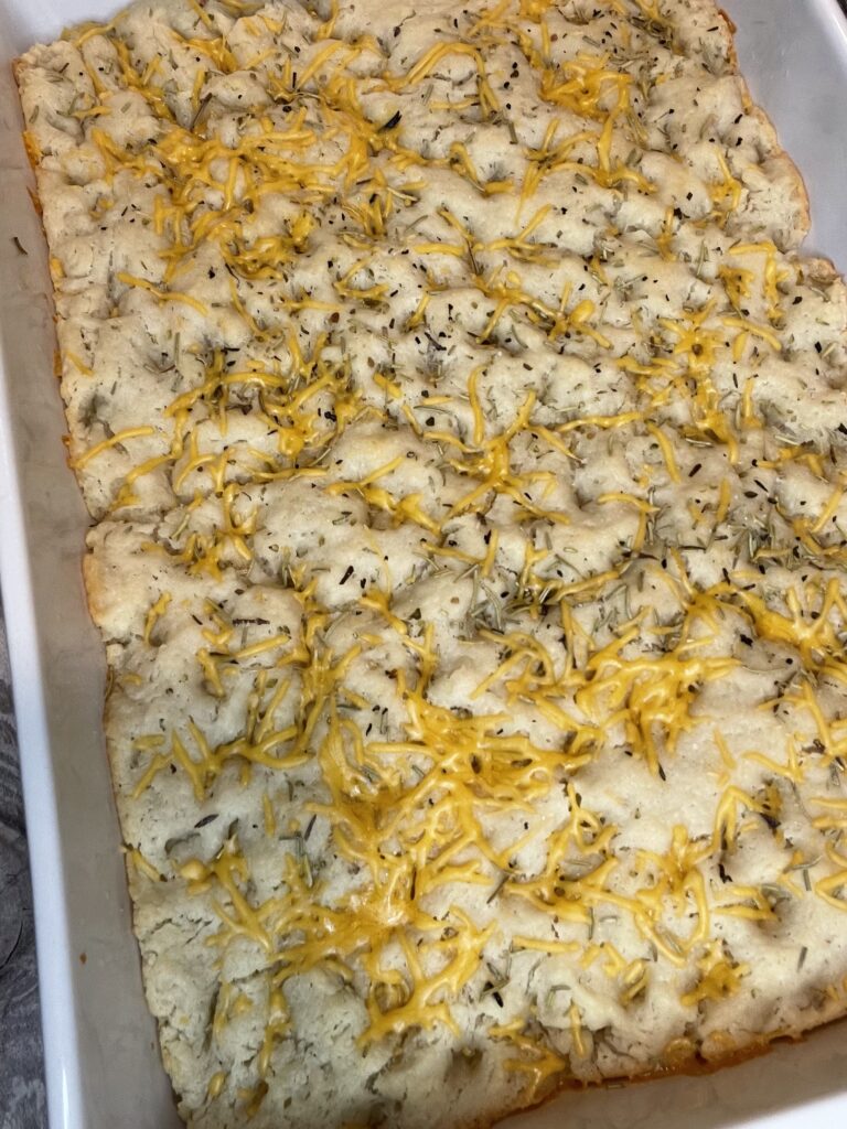 Golden sourdough focaccia fresh from the oven, topped with rosemary, cheese and herb salt